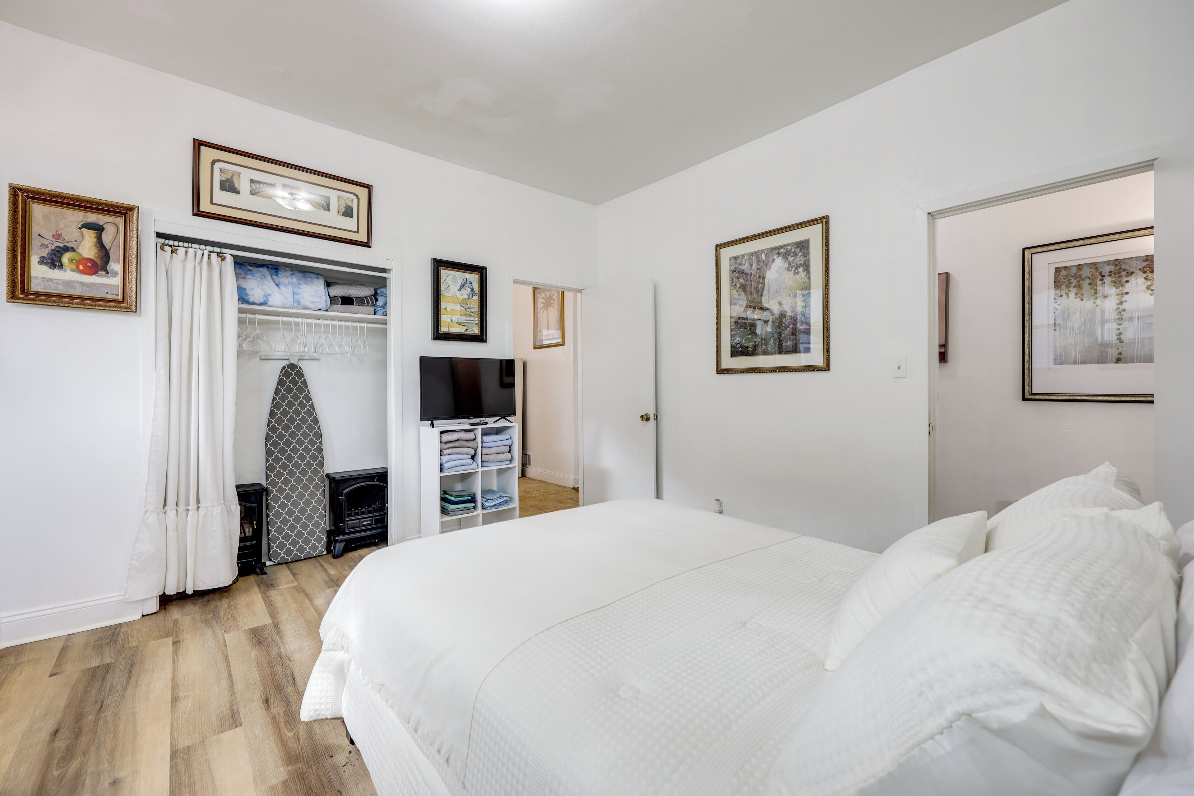 A bedroom with a large bed, a wardrobe, a television, and framed pictures on the wall.