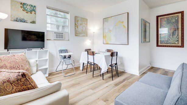 Ein modernes Wohnzimmer mit Fernseher, Essbereich mit Tisch und Stühlen sowie Kunstwerken an den Wänden.