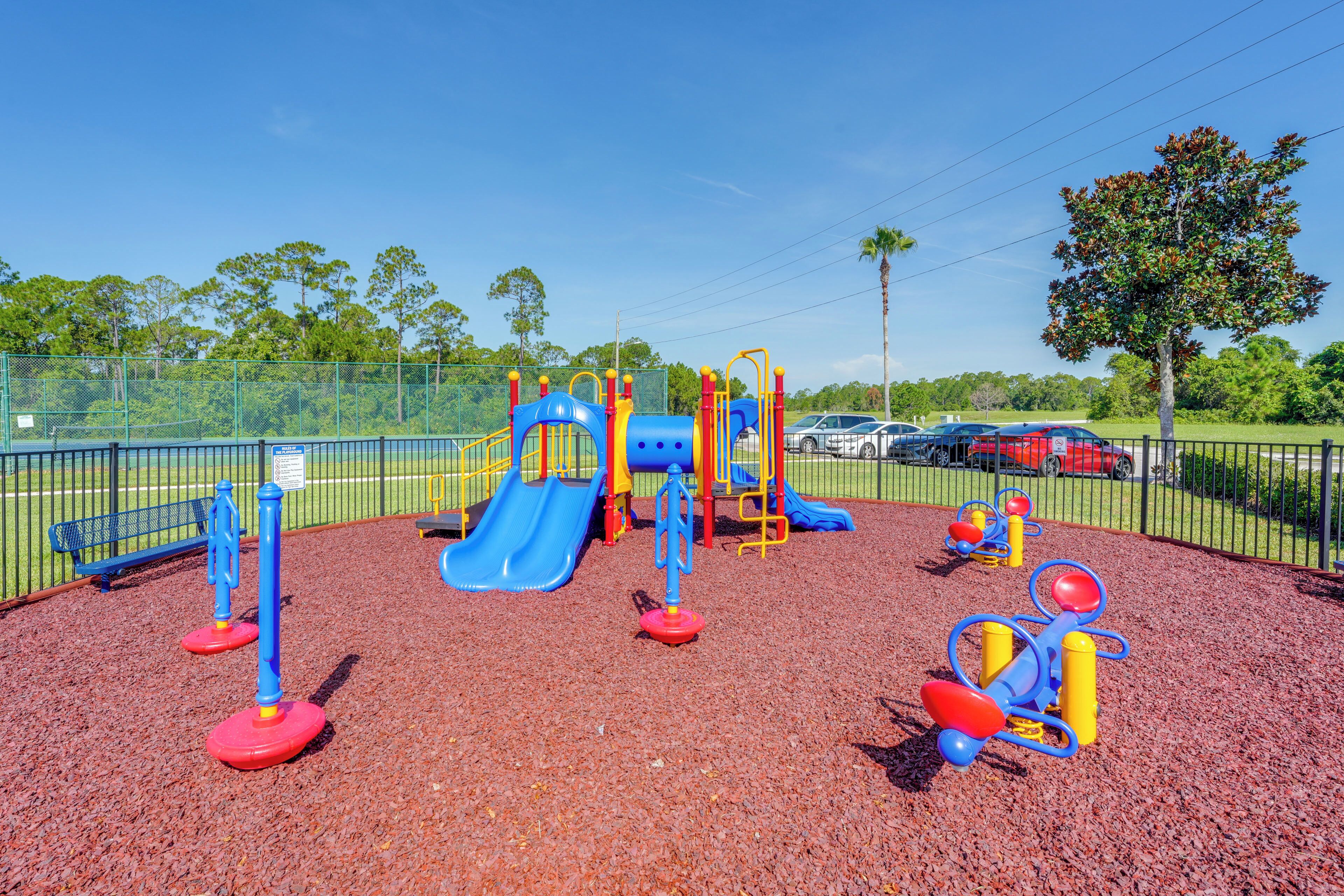 A playground with a blue slide, red and yellow climbing structures, and a fenced area.