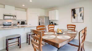 Una cocina moderna con armarios blancos, un refrigerador de acero inoxidable y un comedor con mesa y sillas de madera.