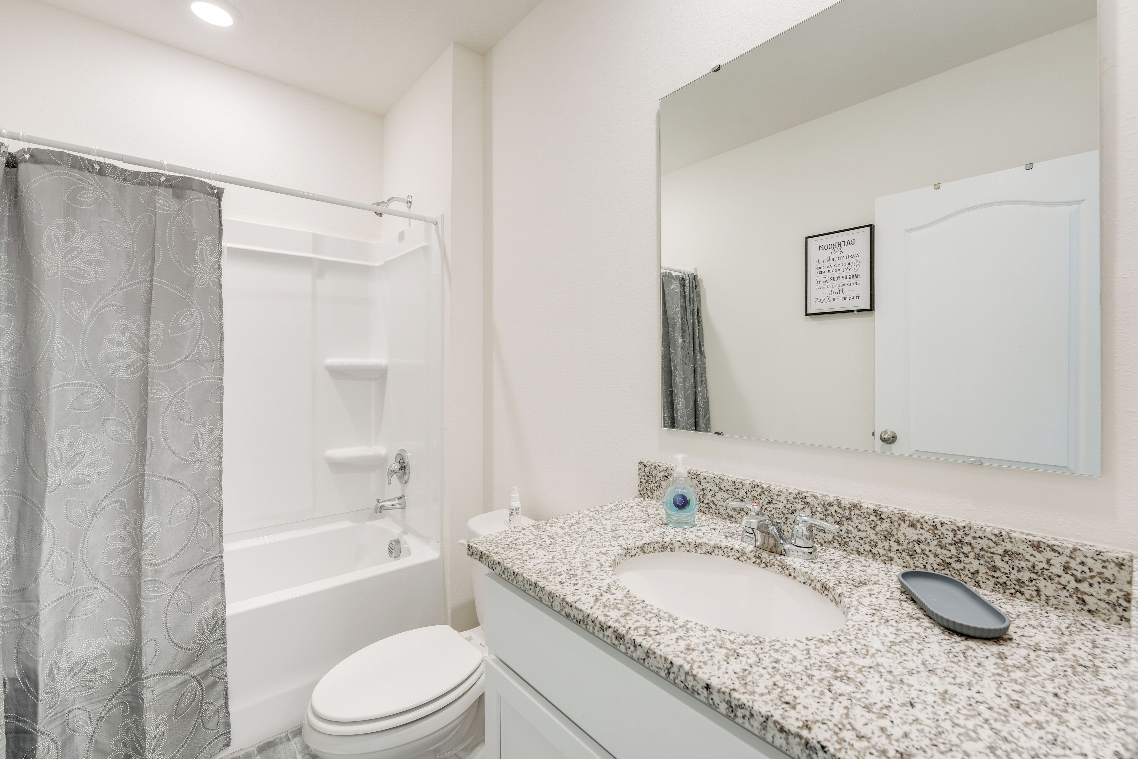 A bathroom with a shower, toilet, sink, and a mirror with a framed picture.