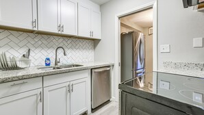 Cocina moderna con armarios blancos, encimera de granito, lavavajillas de acero inoxidable y estufa con puerta de vidrio.