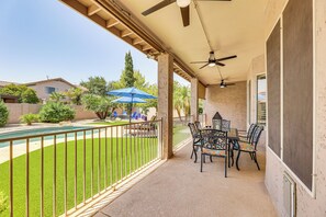 Un patio exterior techado con piscina, una mesa con sillas y una sombrilla azul.