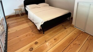 Um quarto com teto de madeira, uma cama com roupa de cama branca, uma pequena mesa de cabeceira e um guarda-roupa.