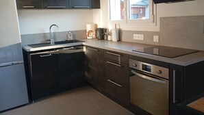 Uma cozinha moderna com armários escuros, eletrodomésticos de aço inoxidável, forno embutido e uma janela que traz luz natural.
