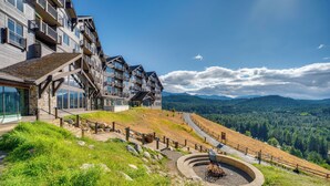 Um hotel com vários andares, varandas, área de estar circular ao ar livre e vista para um vale arborizado.