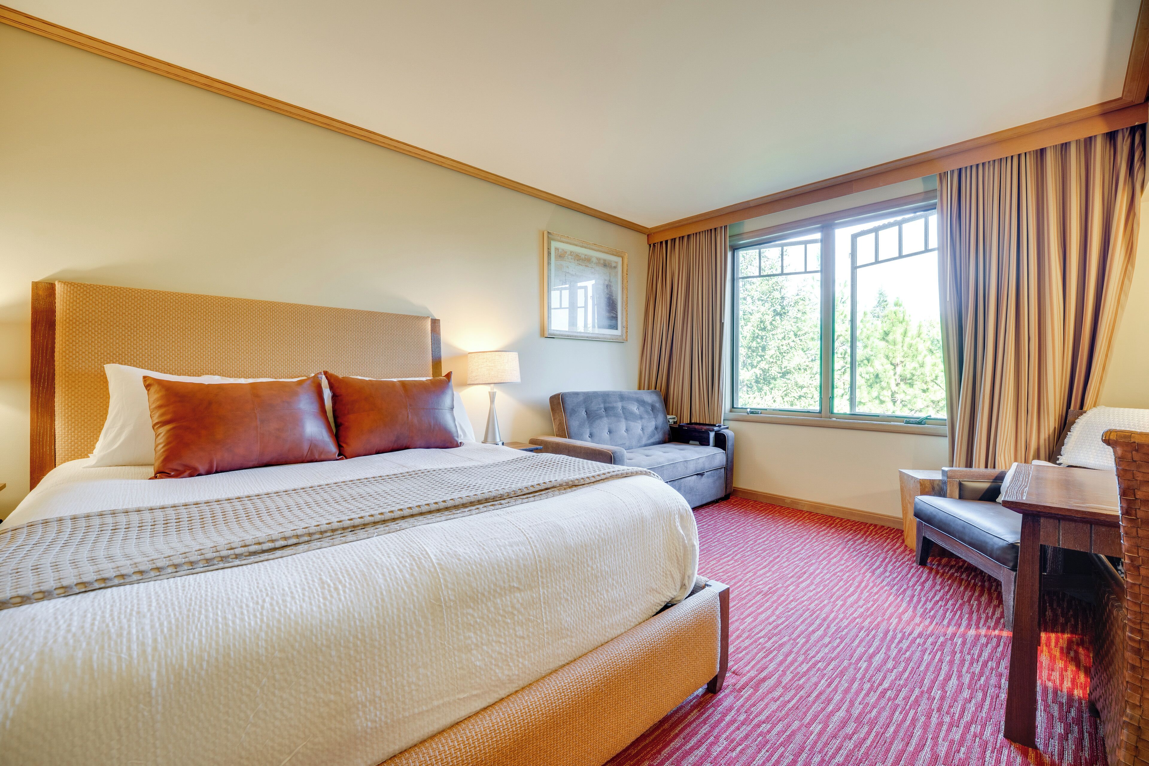 A hotel room with a large bed, a chair, a desk, and a window with curtains.