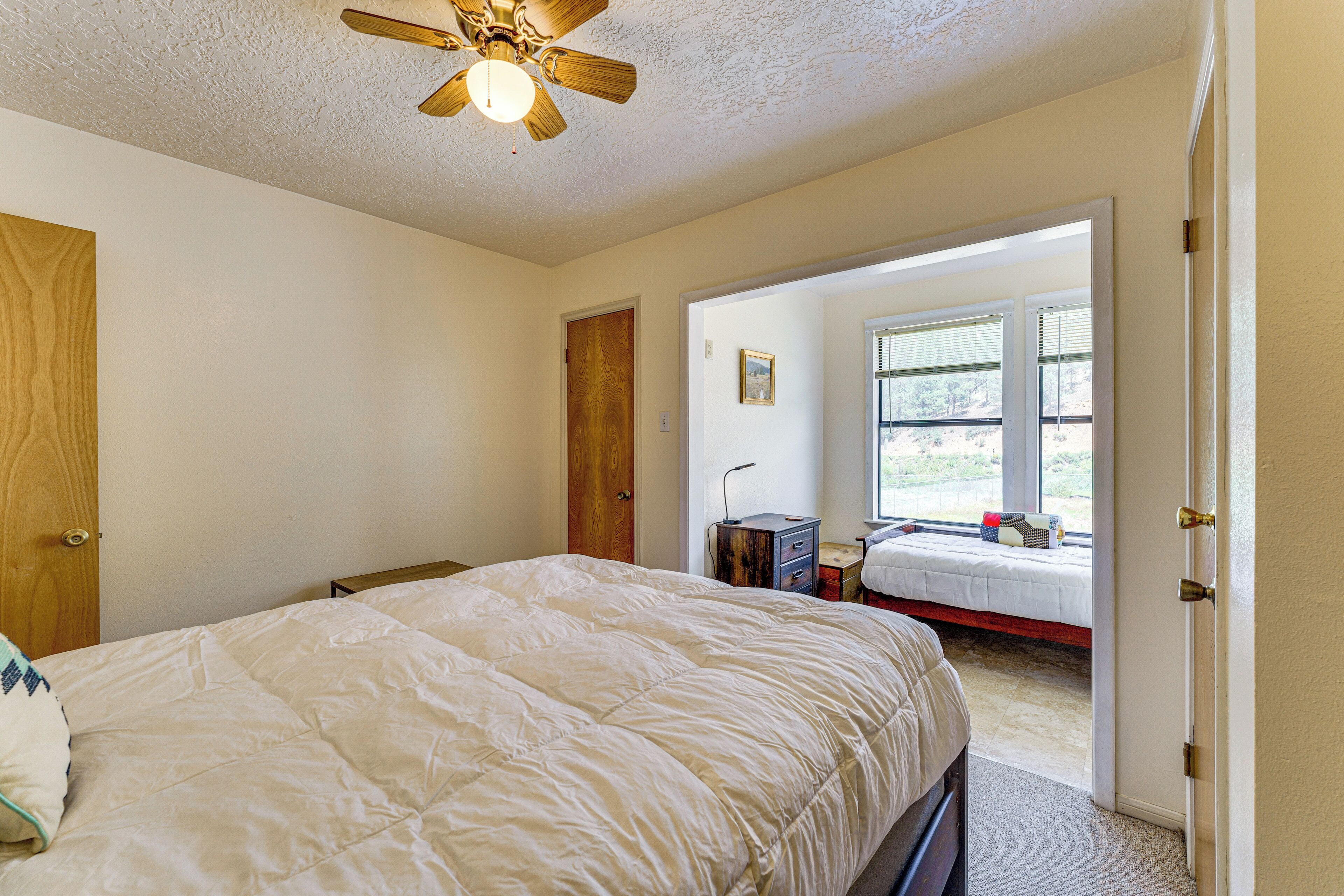 A bedroom with a large bed, a ceiling fan, and a view of the outdoors through a window.