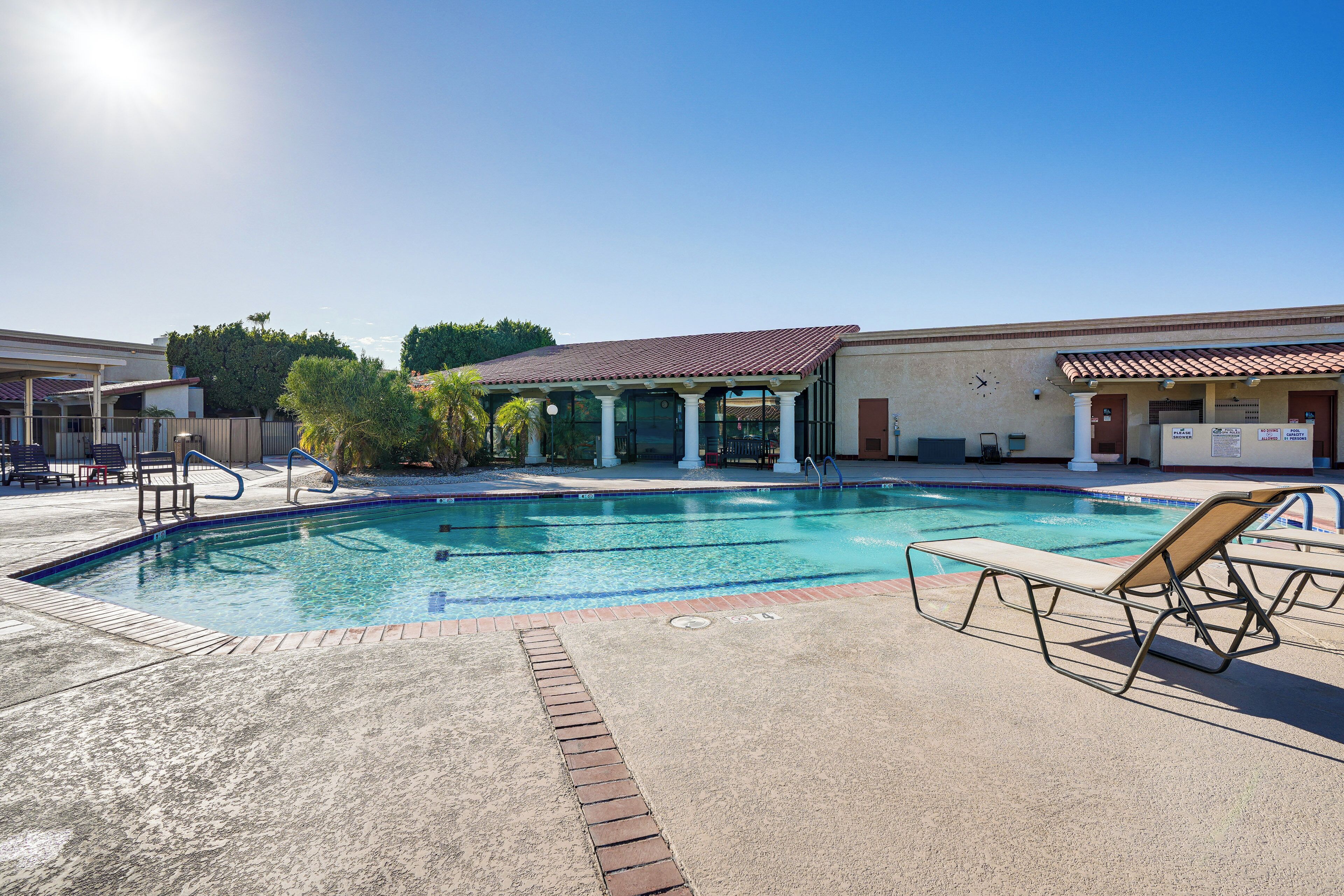 A swimming pool with lounge chairs, a covered seating area, and a building with a clock.