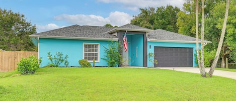 A single-story house with a blue exterior, a front garage, and a well-maintained lawn.