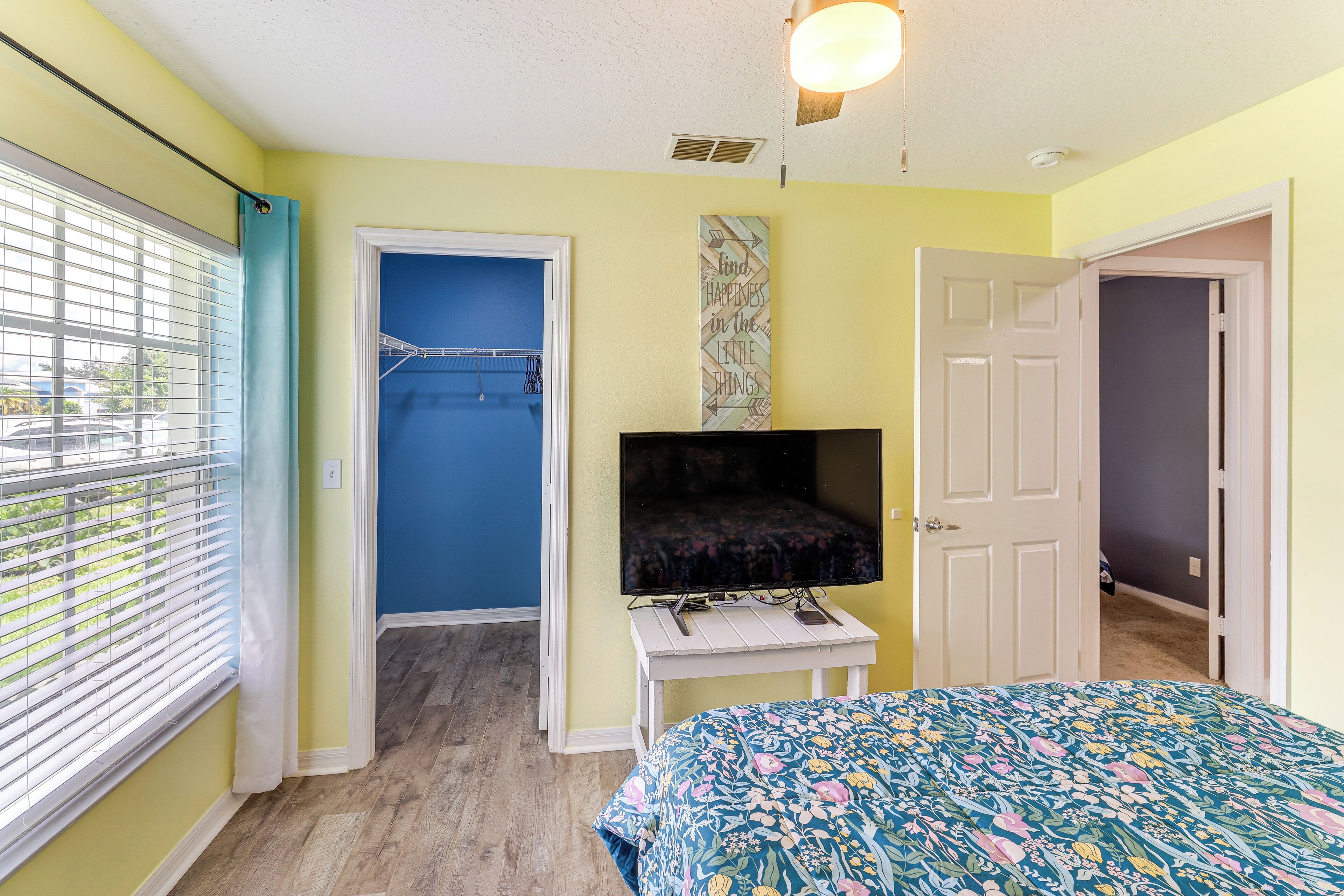 A bedroom with a bed, a television, a door, and a window with blinds.