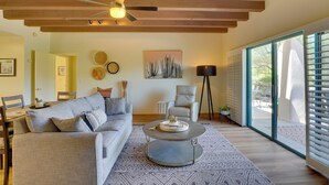 A modern living room with a sofa, coffee table, and a ceiling fan. There is a painting on the wall and a window with blinds. - Amazing Desert Views! Tucson Casita on Golf Course (Tucson)