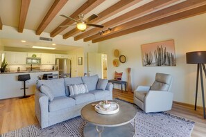 A modern living room with a grey sofa, a round coffee table, and a white armchair. There is a kitchen in the background with white cabinets and a microwave. - Amazing Desert Views! Tucson Casita on Golf Course (Tucson)