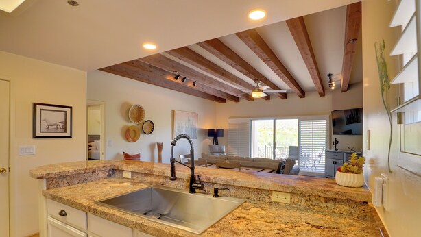 A kitchen with granite countertops, a stainless steel sink, wooden beams on the ceiling, and a dining area visible through a window. - Amazing Desert Views! Tucson Casita on Golf Course (Tucson)