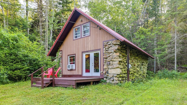 A cabin with a stone foundation, wooden exterior, and a red roof, surrounded by dense forest. - 10 Mi to Gore Mountain! Pet-friendly Cabin (North River)