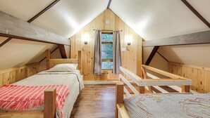 Un dormitorio acogedor en el ático, con techo inclinado, paredes de madera, una ventana con cortinas y una pequeña mesa.
