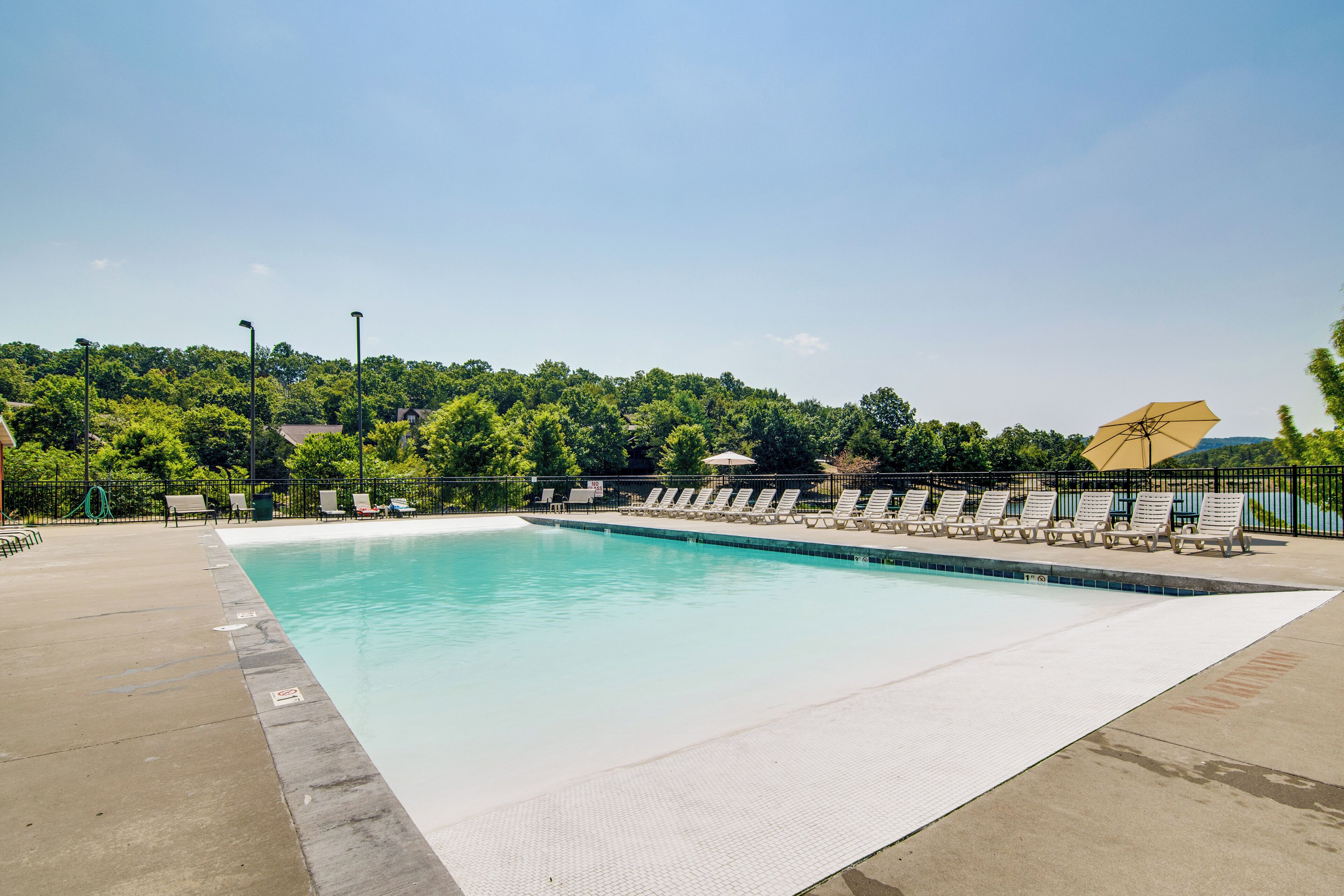 A rectangular swimming pool with a tiled edge, surrounded by lounge chairs and a fence.