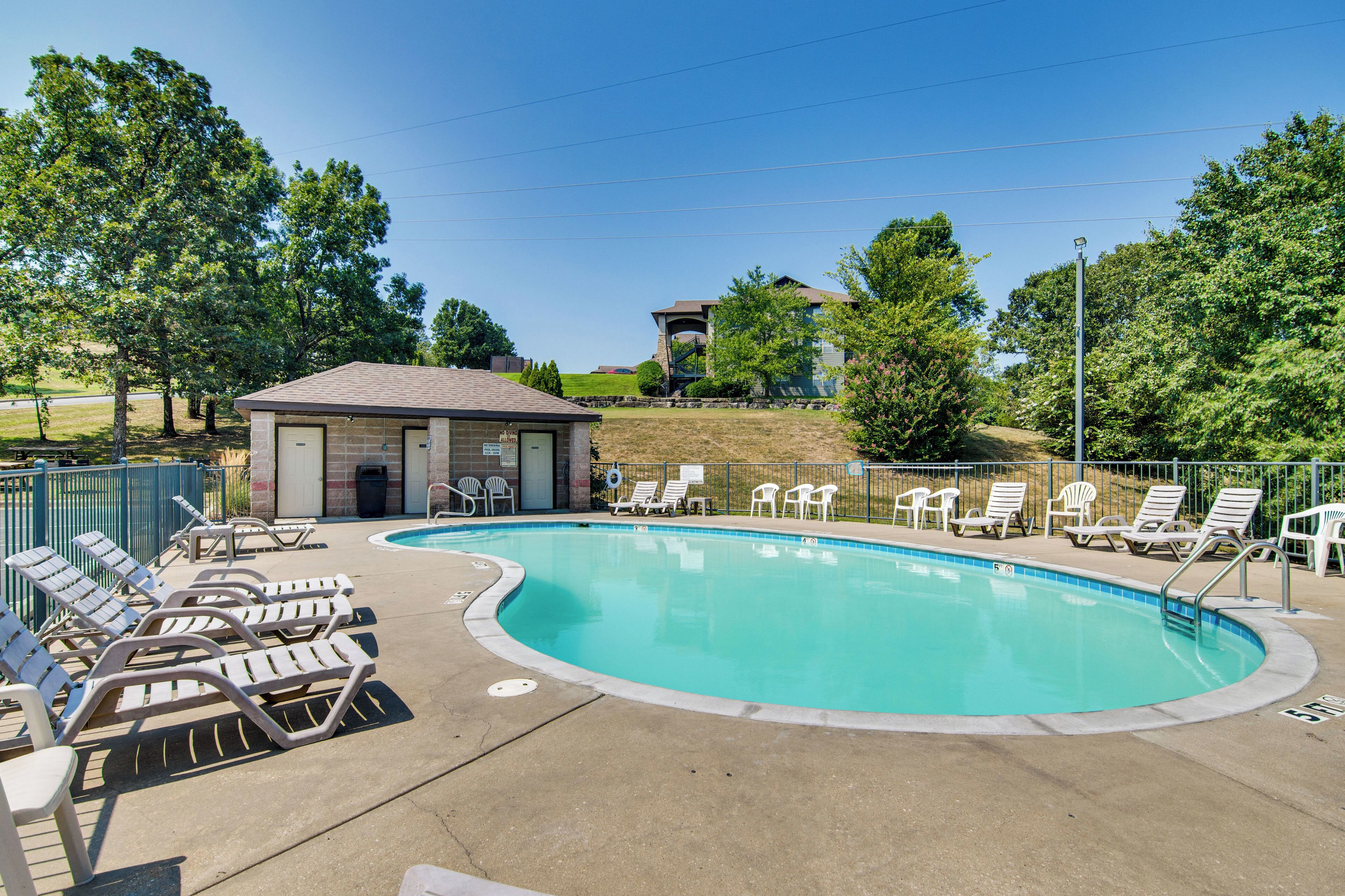 A swimming pool with lounge chairs and a small building, surrounded by trees and a clear sky.