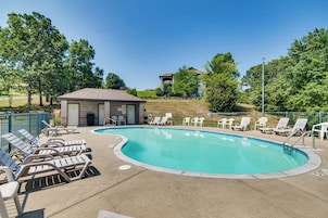 A swimming pool with lounge chairs and a small building, surrounded by trees and a clear sky.