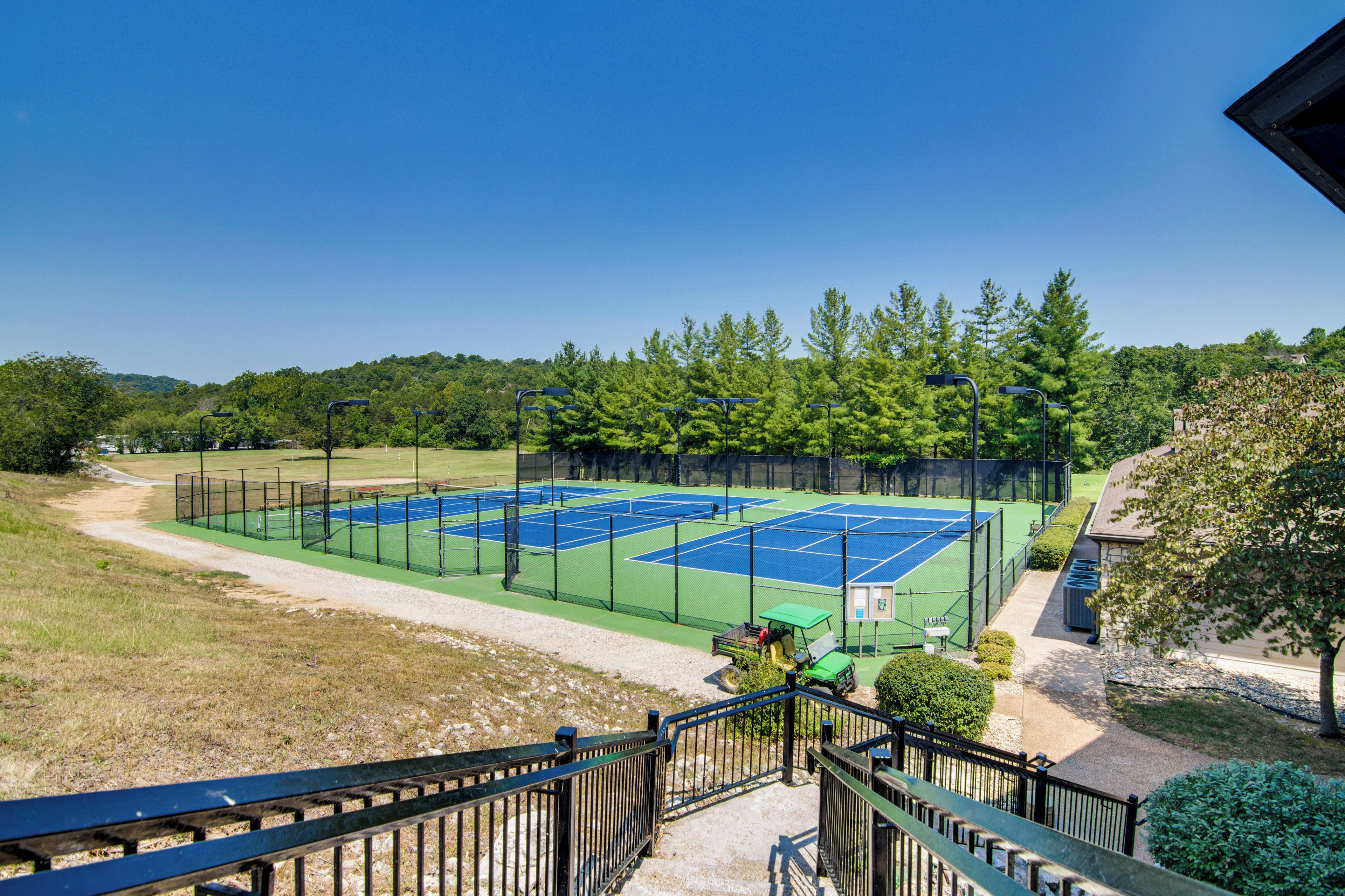 Un complexe de courts de tennis comprenant plusieurs terrains, entouré d’arbres et offrant une vue sur un ciel dégagé.
