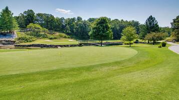 A golf course with a stone bridge, well-maintained grass, and trees in the background.