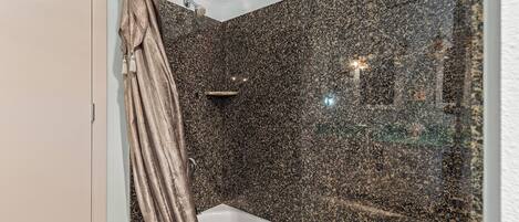 Un baño con una bañera blanca, baldosas oscuras con motas y una zona de ducha, además de una cortina.