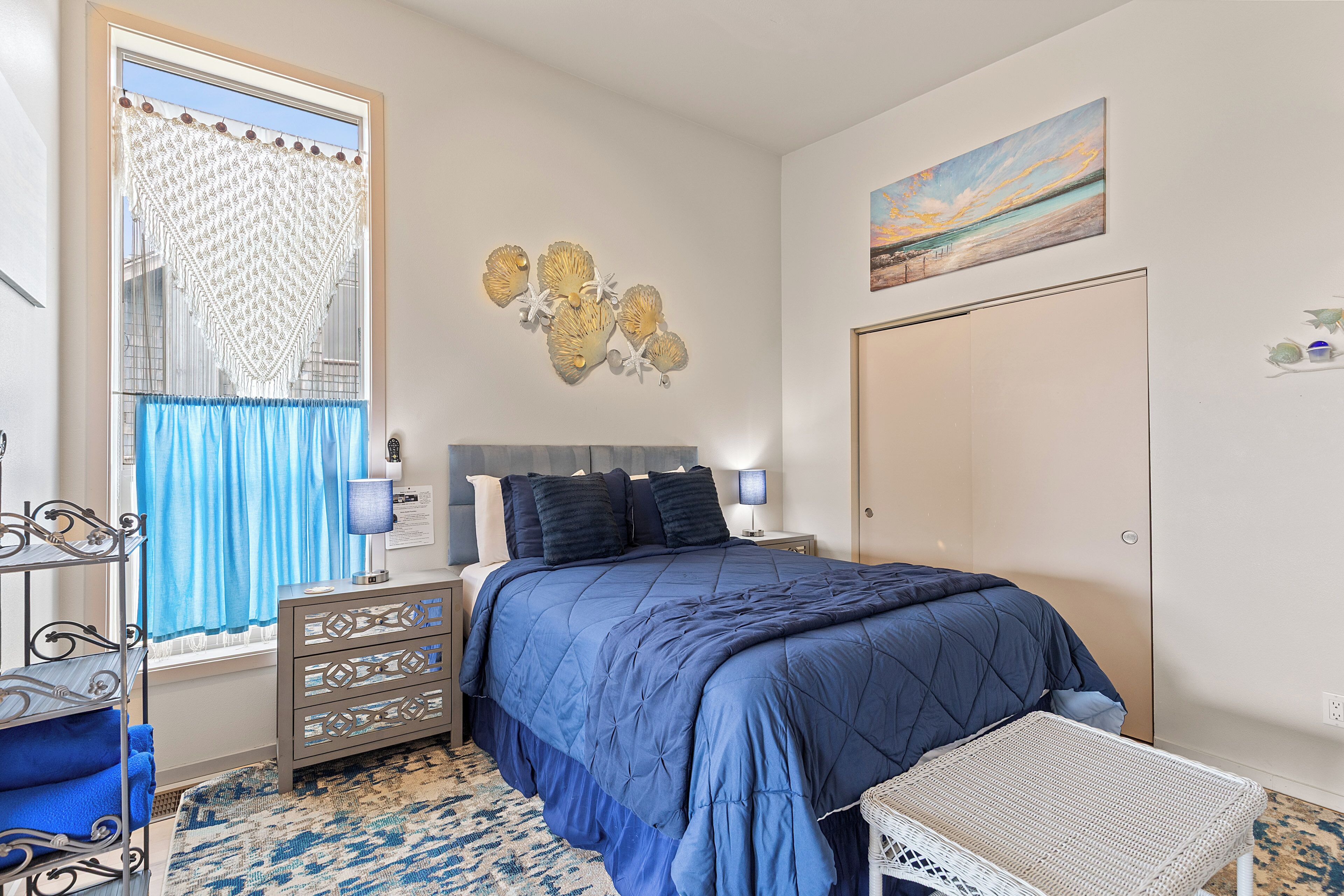 A bedroom with a bed, a dresser, a window with curtains, a wall art piece, and a door.