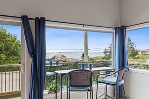 A balcony with a table and chairs, overlooking a rocky coastline and greenery.