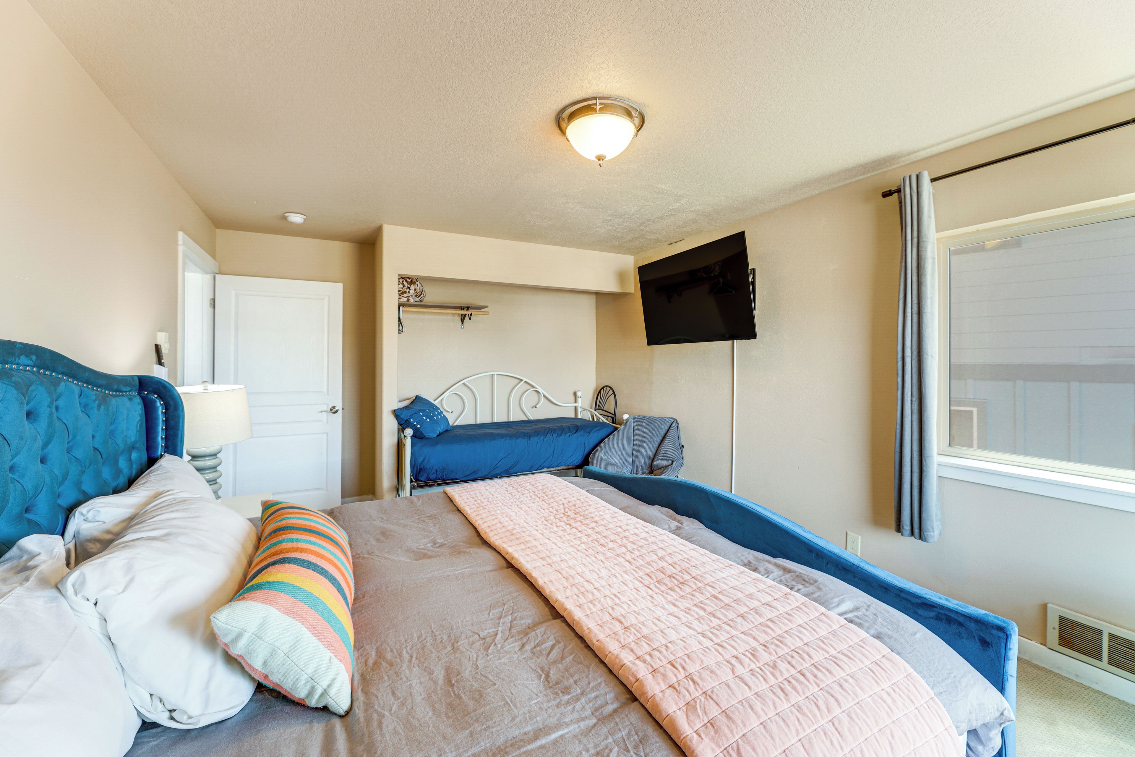 A bedroom with a bed, a bedside table, a lamp, a TV mounted on the wall, and a window with curtains.