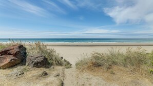 Una playa con cielo despejado, orilla arenosa y rocas grandes al frente.