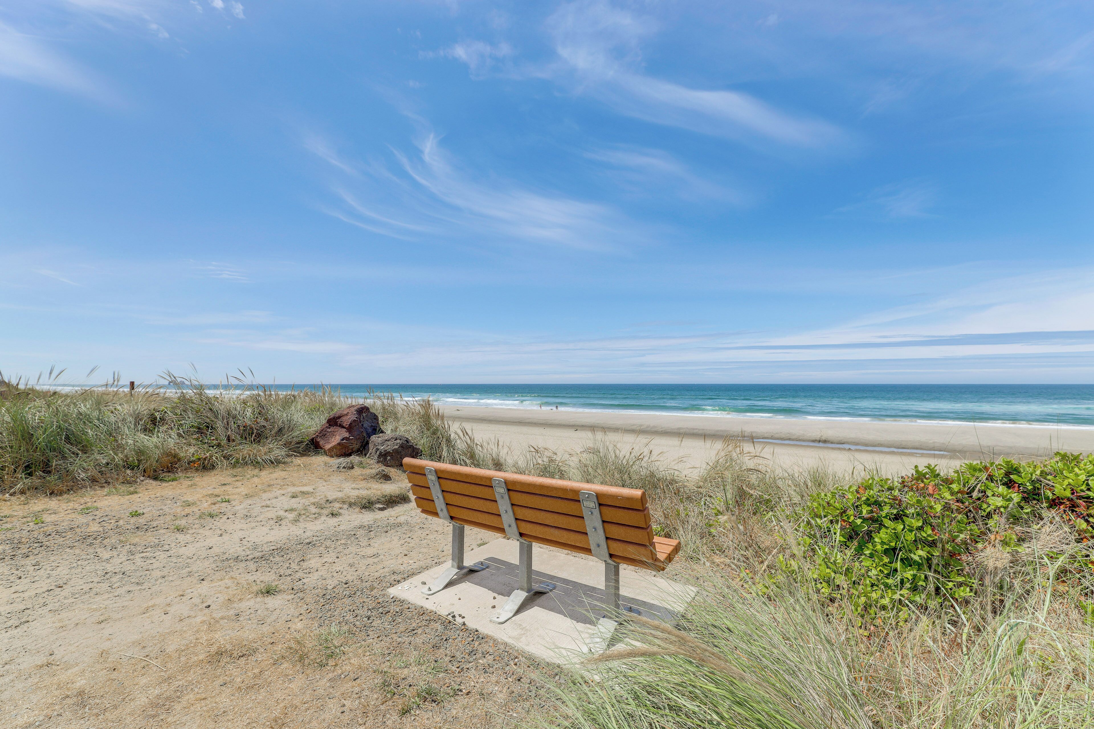 A bench on a sandy beach with the ocean in the background.