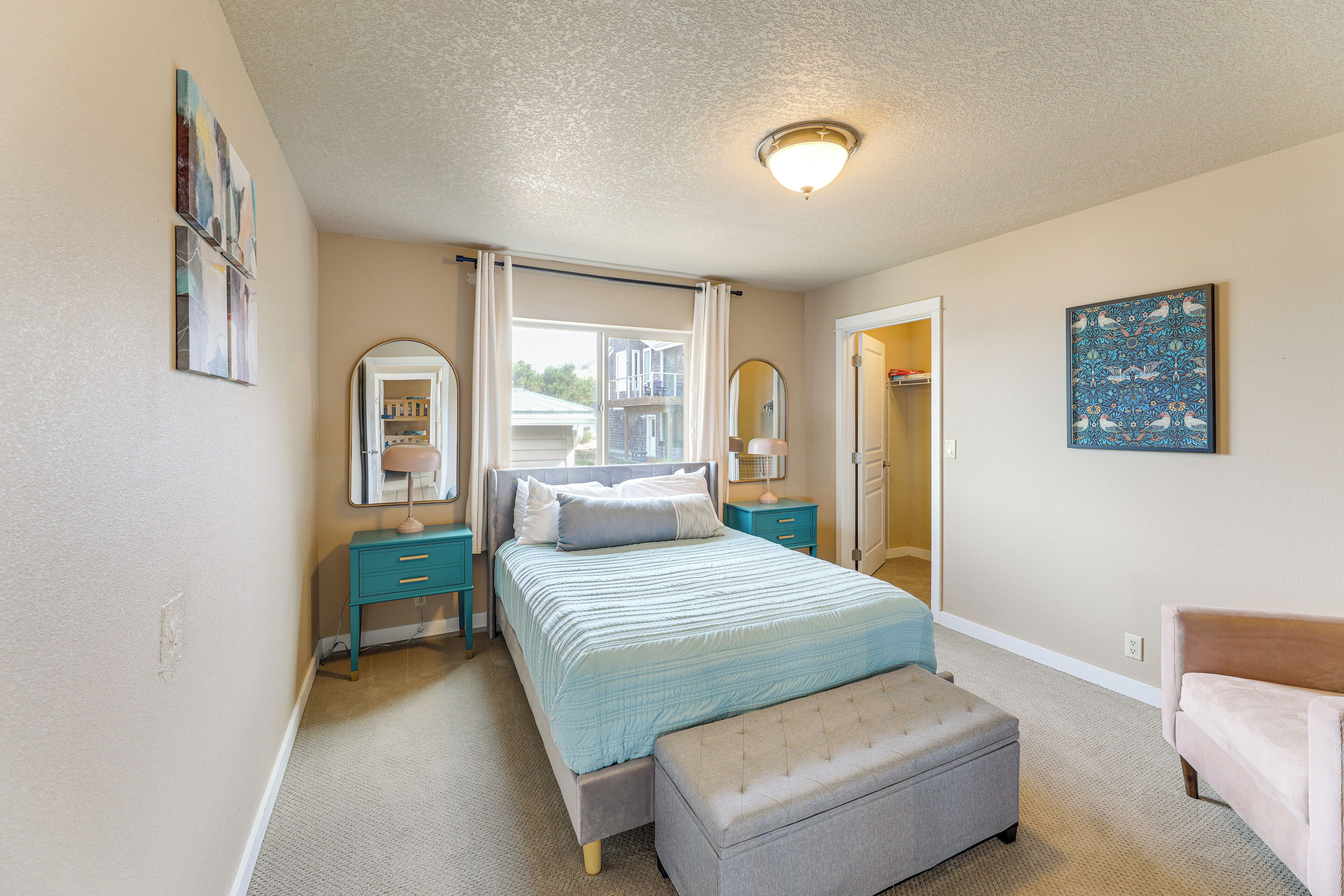 A bedroom with a bed, bedside tables, a bench, a mirror, and artwork on the walls.