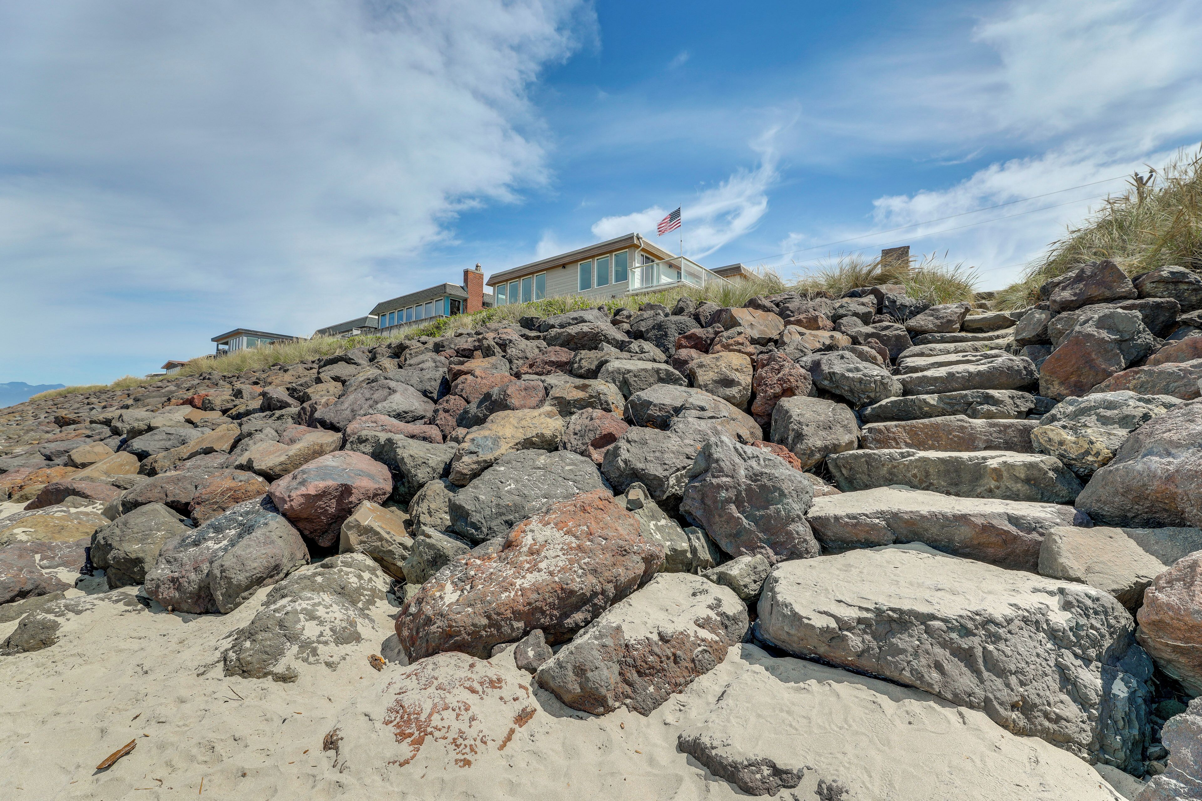 Une maison située sur la côte, avec un drapeau, entourée de gros rochers et de sable.