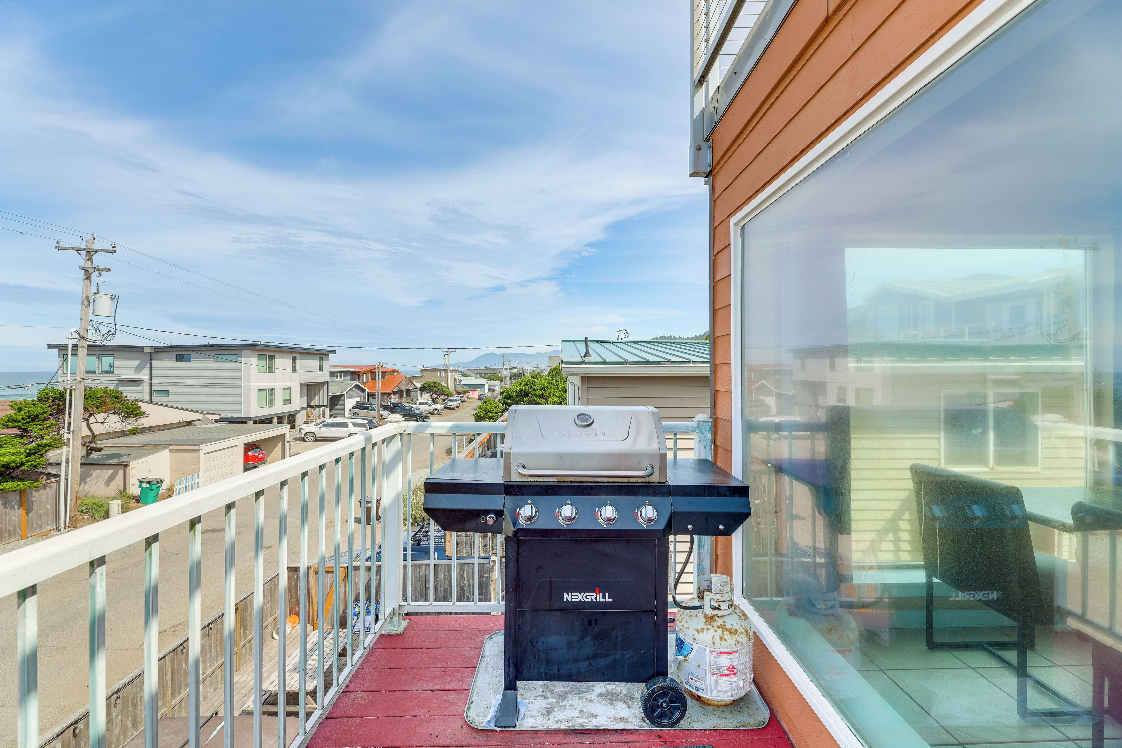 Een balkon met een barbecue en gasfles, met uitzicht op een woonwijk.