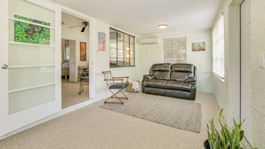 A spacious living room with a leather sofa, a dining table, and a chair. There is a window with blinds, a ceiling fan, and artwork on the walls.