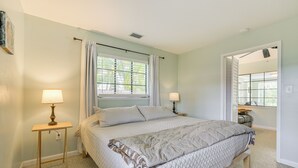 A bedroom with a bed, two bedside lamps, a window with curtains, and a door leading to another room.
