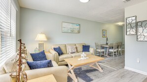 A living room with a beige sofa, a wooden coffee table, and a dining area with a table and chairs. - 2 Mi to State Park: Dog-friendly Niceville Home (Niceville)