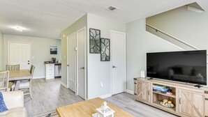 A living room with a wooden coffee table, a television on a wooden stand, and a kitchen area in the background. - 2 Mi to State Park: Dog-friendly Niceville Home (Niceville)