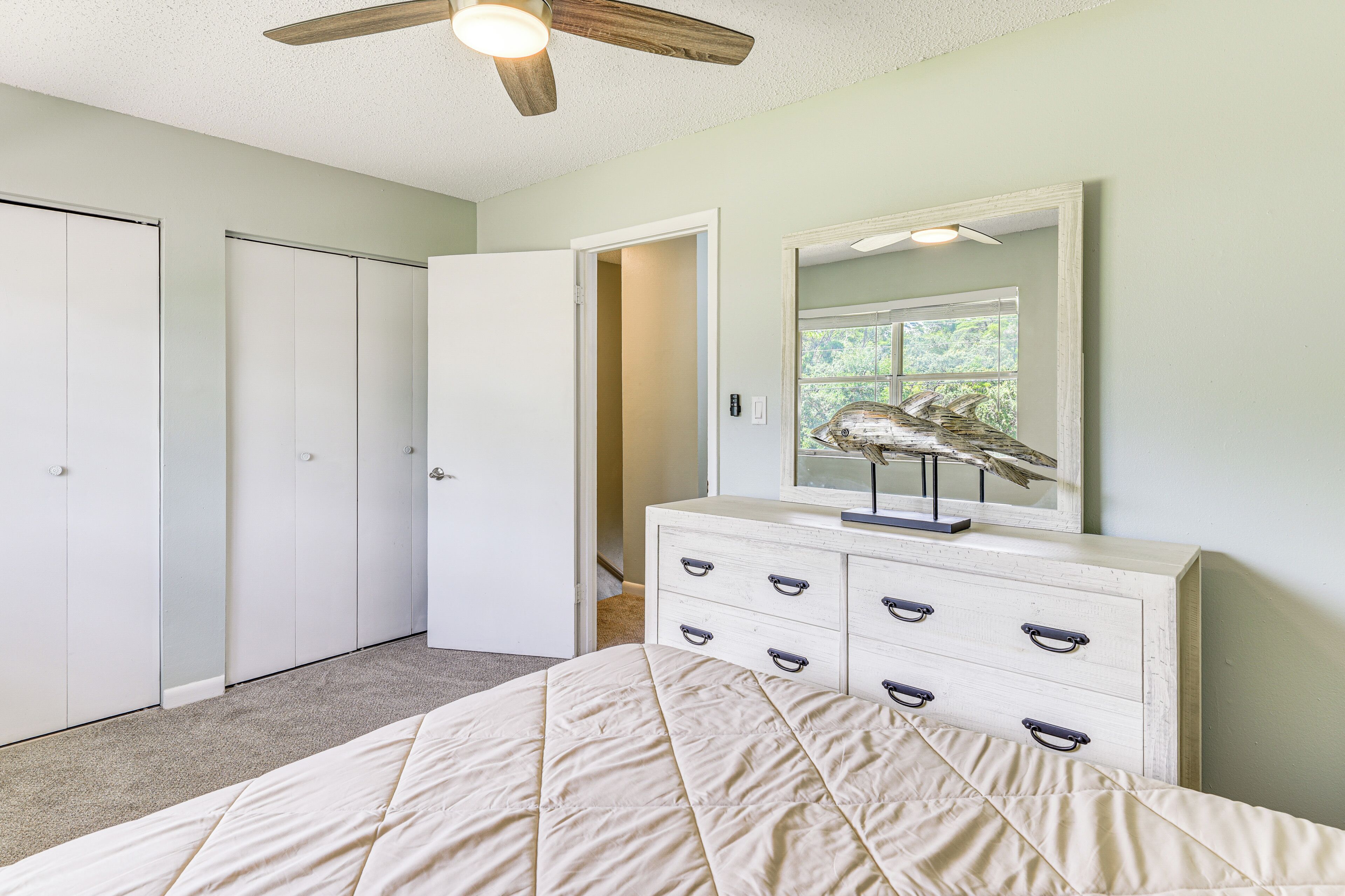 Un dormitorio con cama, cómoda, ventilador de techo y puerta que da a otra habitación.