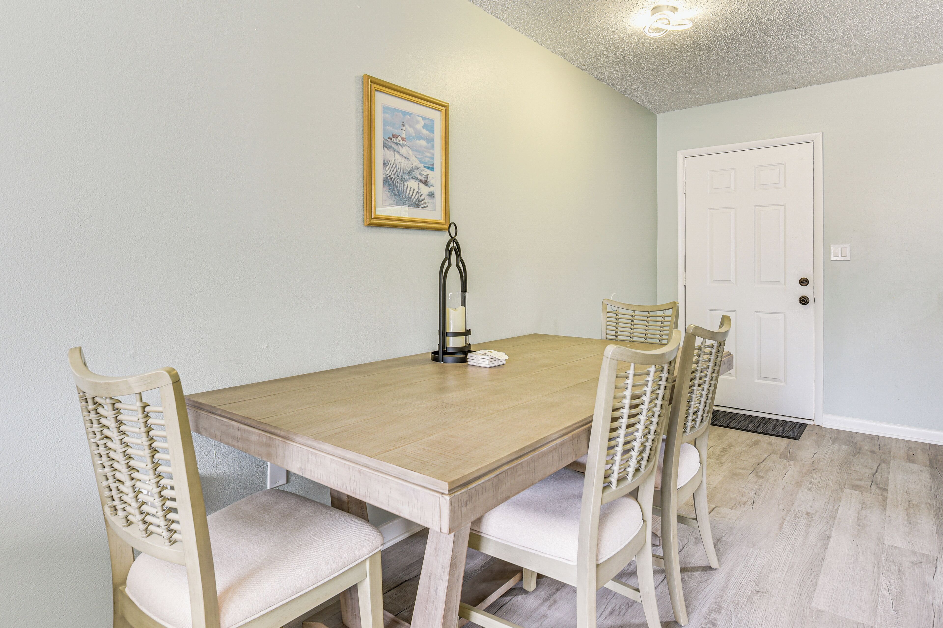 Een eetruimte met een houten tafel en stoelen, een lijst met een foto aan de muur, en een witte deur.