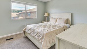 A bedroom with a bed, a nightstand, a lamp, and a window with a view of buildings. - 2 Mi to State Park: Dog-friendly Niceville Home (Niceville)
