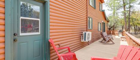 A wooden cabin with a deck, a door, and two rocking chairs.