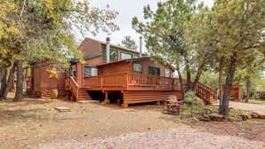A rustic log cabin with a deck, surrounded by trees.