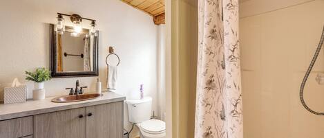 A bathroom with a wooden ceiling, a sink with a mirror, a toilet, and a shower with floral curtains.