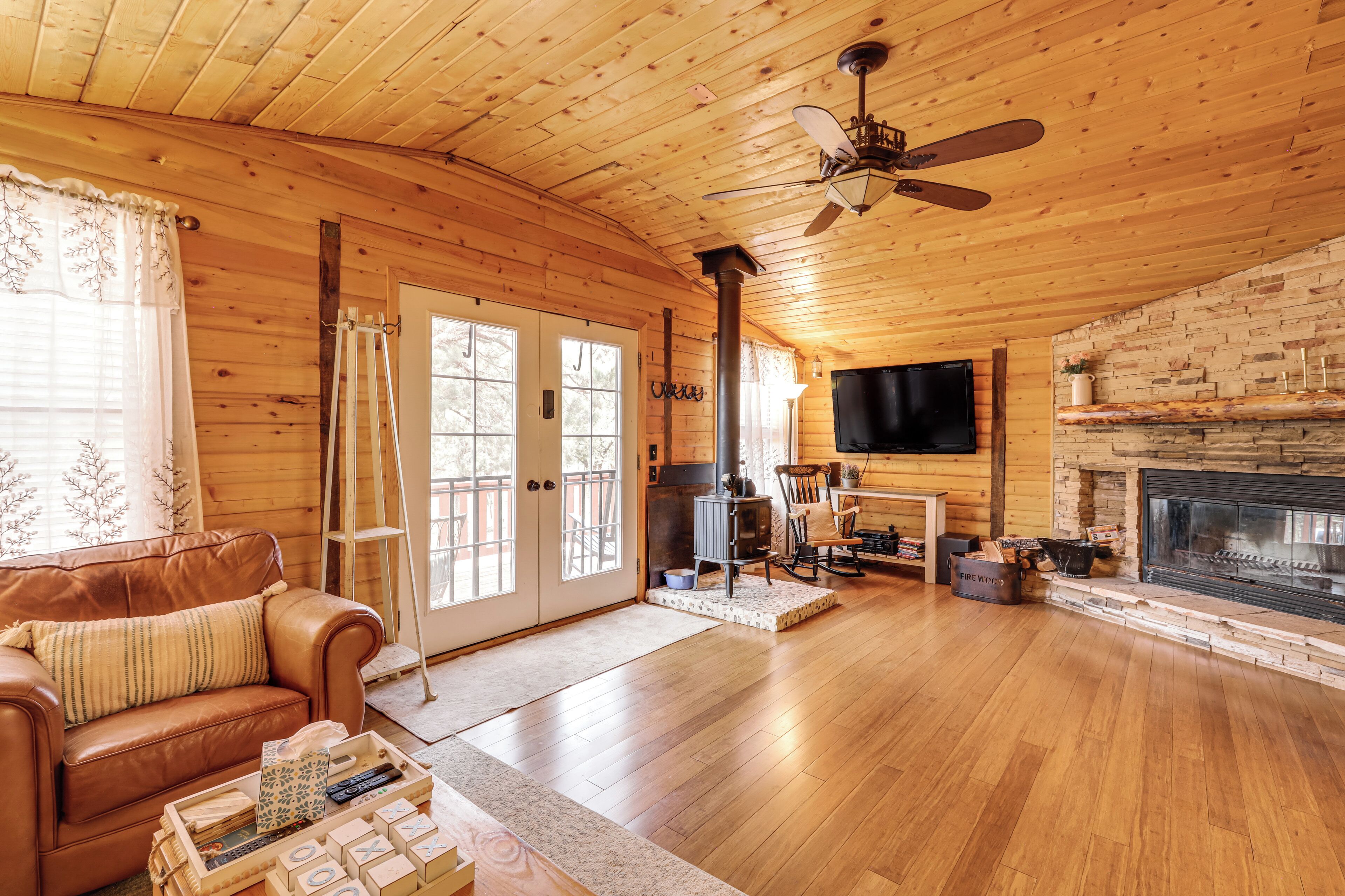 A cozy cabin interior with a wooden interior, a fireplace, a television mounted on the wall, and a leather sofa.