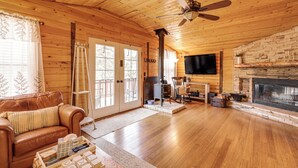 A cozy cabin interior with a wooden interior, a fireplace, a television mounted on the wall, and a leather sofa.
