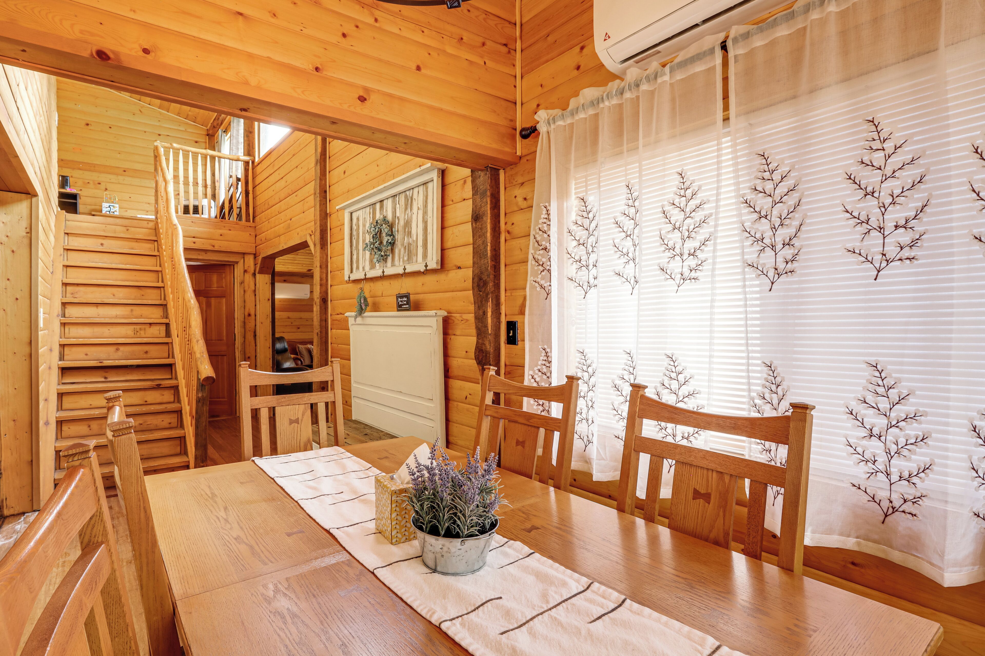 Un intérieur en bois comprenant une table à manger, des chaises, un escalier et une fenêtre agrémentée de rideaux décoratifs.