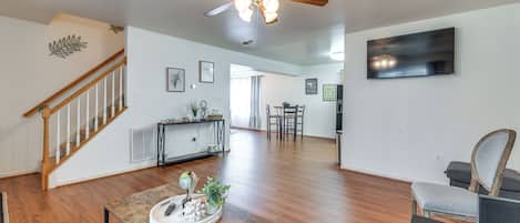 Amplia sala de estar con pisos de madera, una mesa de centro de madera, un ventilador de techo, una escalera y un área de comedor al fondo.