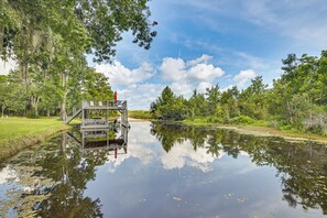 Un cadre paisible au bord de la rivière, avec un quai en bois et une petite plateforme, le tout entouré d’une végétation luxuriante et d’arbres.