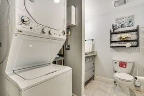 A laundry area with a front-loading washer and dryer, a bathroom with a toilet, and a shelf with decorative items. - Withlacoochee River Retreat w/ Dock: Paddle & Fish (Citrus Springs)